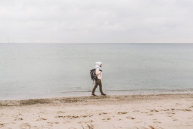 Bir beyaz adam genç Kafkas kadın turist kışın Baltık Denizi yakınında kumlu bir plaj üzerinde siyah bir sırt çantası ile. Tema yolculuk yalnız. Düşünce ve hayalleri ufuk bakan