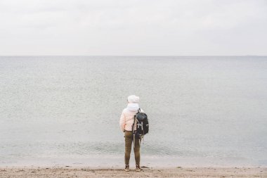 Bir beyaz adam genç Kafkas kadın turist kışın Baltık Denizi yakınında kumlu bir plaj üzerinde siyah bir sırt çantası ile. Tema yolculuk yalnız. Düşünce ve hayalleri ufuk bakan