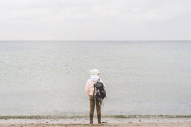 Bir beyaz adam genç Kafkas kadın turist kışın Baltık Denizi yakınında kumlu bir plaj üzerinde siyah bir sırt çantası ile. Tema yolculuk yalnız. Düşünce ve hayalleri ufuk bakan