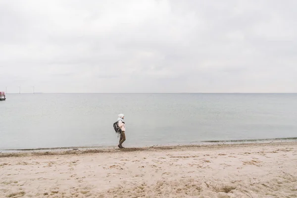 Un hombre caucásico joven turista caucásico con una mochila negra en una playa de arena cerca del mar Báltico en invierno. Viaje temático solo. Pensamientos y sueños con vistas al horizonte —  Fotos de Stock