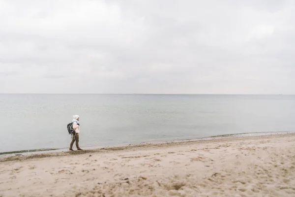 One caucasian man young caucasian woman tourist with a black backpack on a sandy beach near the Baltic sea in winter. Theme trip alone. Thoughts and dreams overlooking the horizon — Stock Photo, Image