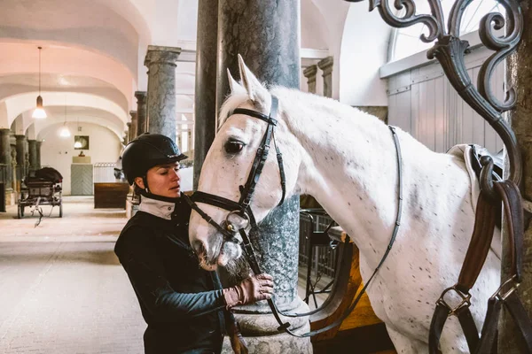 Şubat 20, 2019.Royal bölge Christiansborg yuvası Danimarka Kopenhag ahırda. Adam genç kadın binici jokey hazırlanması için bir at başlığı, at başlığı, fırsat, bridel snaffle, dizgin beyaz atlı