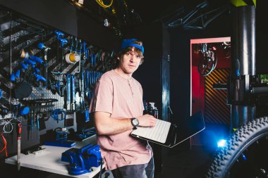 Tema iş meslek yönetici ve teknoloji. Tamir ve bisiklet bakımı için bir dizüstü bilgisayar standı yakınındaki genç şık beyaz erkek sahibi Bisiklet dükkanı ile araçlarını kullanır