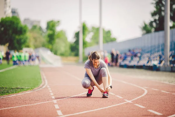 Tema spor ve spor giyim. Ayarlama Tekdüzen bağlama ayakkabı bağcığı genç bir beyaz kadın bir stadyumda bir koşu bandı parça spor ayakkabı ayakkabı