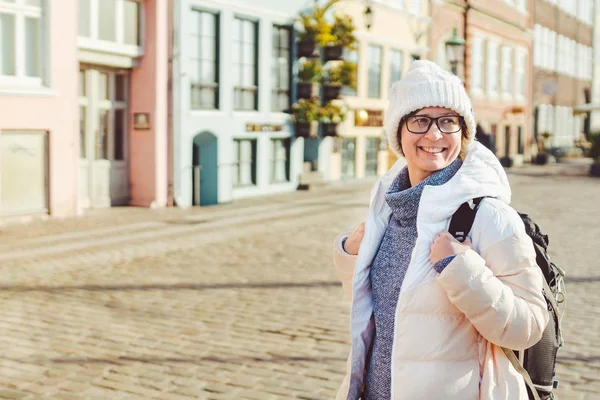 Retrato de una joven turista europea caucásica en gafas para la vista de un sombrero blanco y una chaqueta con una mochila negra posando en una antigua calle de Europa en la ciudad de Copenhague en Dinamarca — Foto de Stock