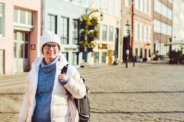 Retrato de uma jovem mulher europeia caucasiana turista de óculos para a vista de um chapéu branco e uma jaqueta com uma mochila preta posando em uma antiga rua da Europa na cidade de Copenhague, na Dinamarca — Fotografia de Stock