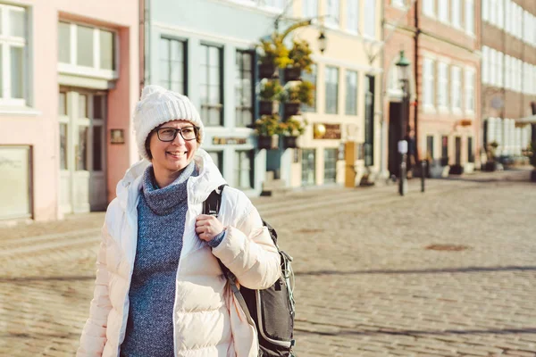 Retrato de una joven turista europea caucásica en gafas para la vista de un sombrero blanco y una chaqueta con una mochila negra posando en una antigua calle de Europa en la ciudad de Copenhague en Dinamarca — Foto de Stock