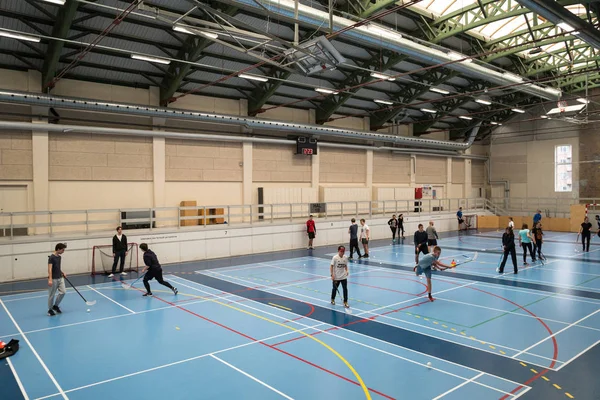 February 21, 2019. Denmark. Copenhagen. Team game with stick and ball Floorball or hockey in hall. Inside training in the gym of the school college. Group of teen caucasian students playing a game — Stock Photo, Image