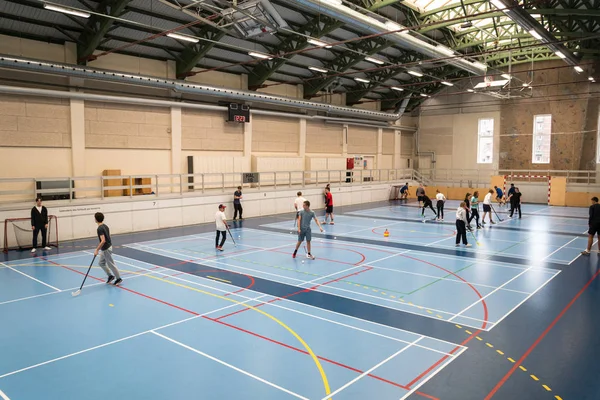 21 de fevereiro de 2019. Dinamarca. Copenhaga. Jogo de equipe com vara e bola Floorball ou hóquei no salão. Treinamento interno no ginásio da faculdade da escola. Grupo de adolescentes estudantes caucasianos jogando um jogo — Fotografia de Stock