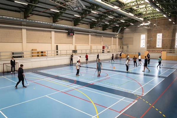 February 21, 2019. Denmark. Copenhagen. Team game with stick and ball Floorball or hockey in hall. Inside training in the gym of the school college. Group of teen caucasian students playing a game — Stock Photo, Image