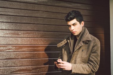 Genç yakışıklı Türk erkek model ahşap duvar çerçevede güneşli havalarda sokakta el telefon teknolojisi işadamı kullanarak deri ceket Akdeniz yarış brunet portresi