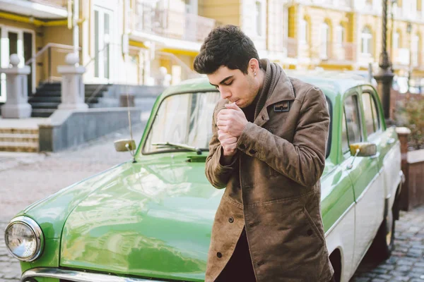 Portrait of a model young handsome sexy male brunette guy with dark skin Turkish Middle Eastern brunette posing smoking a cigarette near old retro car on the street