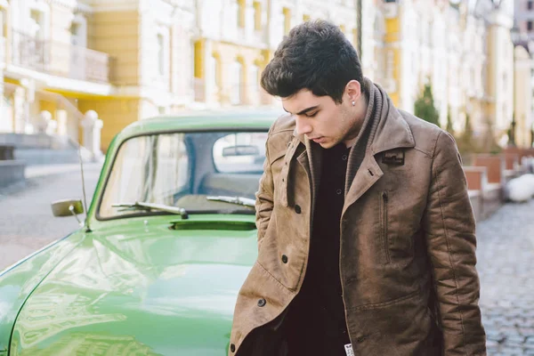 Portrait of a model young handsome sexy male brunette guy with dark skin Turkish Middle Eastern brunette posing smoking a cigarette near old retro car on the street — Stock Photo, Image