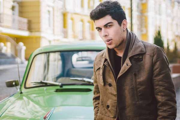 Retrato de una modelo joven guapo morena masculina sexy con piel oscura morena turca de Oriente Medio posando fumando un cigarrillo cerca de viejo coche retro en la calle —  Fotos de Stock
