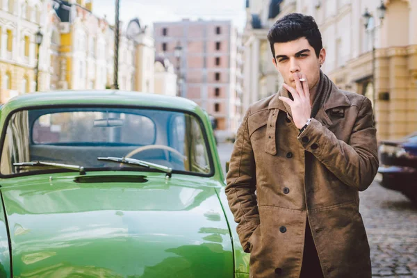 Portrait of a model young handsome sexy male brunette guy with dark skin Turkish Middle Eastern brunette posing smoking a cigarette near old retro car on the street