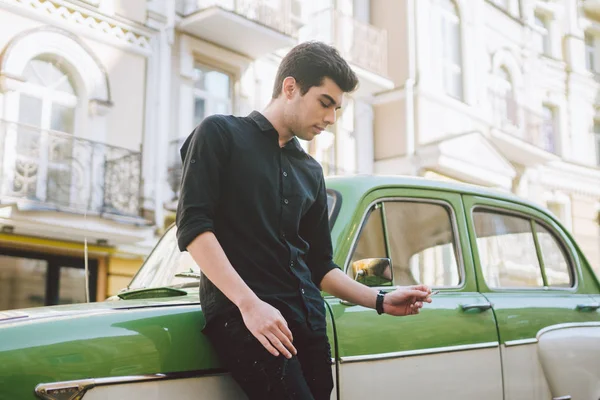 Portrait of a model young handsome sexy male brunette guy with dark skin Turkish Middle Eastern brunette posing smoking a cigarette near old retro car on the street