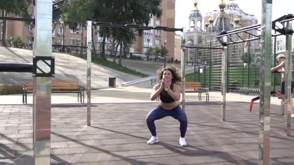 Tema sport och hälsosam livsstil. Unga kaukasiska kvinna med lockigt hår tatoo idrottsman gör träning muskler i benen och skinkor. Flicka crouches och hoppar på webbplatsen urban träning — Stockvideo