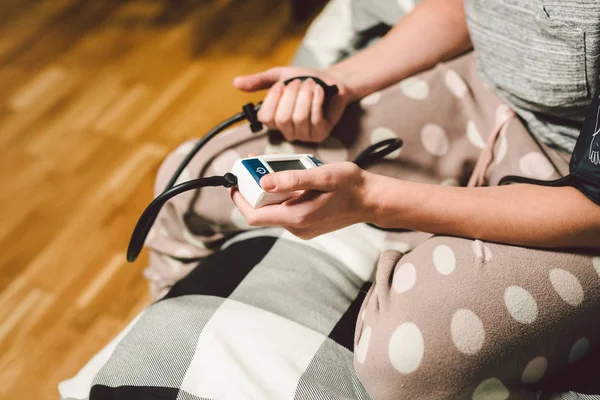 Il tema della pressione alta è la malattia da ipertensione. Primo piano macro giovane donna caucasica mani utilizzando tonometro automatico per controllare la pressione a casa in camera da letto sul letto — Foto Stock