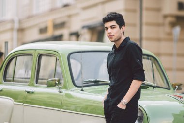 portre, yakışıklı, erkek, model, esmer Akdeniz ırkı Türk adam siyah tişört ve kot şehrin poz yeşil renkteki bir retro car yakınındaki standları