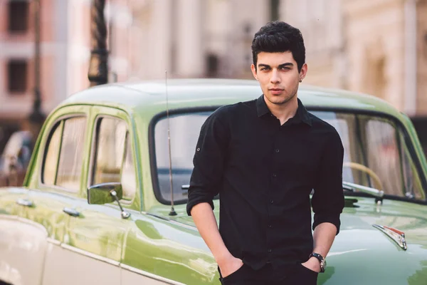 Portrait, handsome, male, model, brunette Mediterranean race Turkish man stands near a retro car of green color posing in a black shirt and jeans in the city — Stock Photo, Image