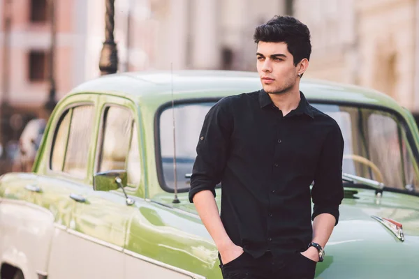 Retrato, guapo, hombre, modelo, morena raza mediterránea hombre turco se encuentra cerca de un coche retro de color verde posando en una camisa negra y jeans en la ciudad —  Fotos de Stock