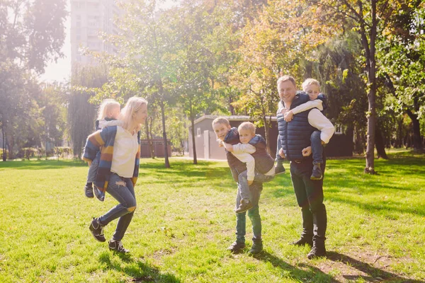 Thema familie actieve vrije tijd buiten in de natuur. grote blanke familie met vier kinderen. Pappa en mamma actief ontspannen. genieten van het leven in het park in de buurt van huis op gras. Kinderen op achterkant schouders roll bovenop — Stockfoto