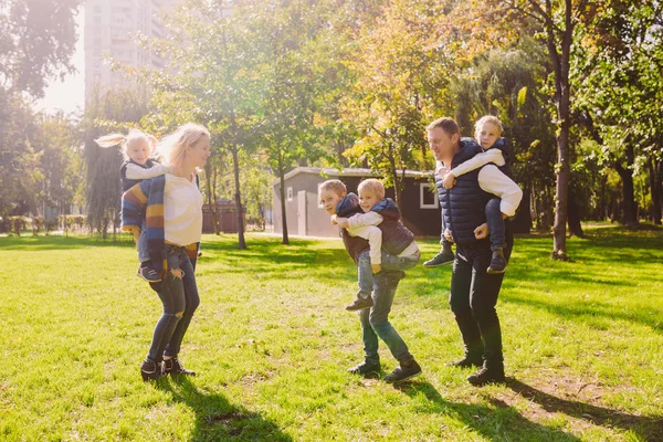 Thema familie actieve vrije tijd buiten in de natuur. grote blanke familie met vier kinderen. Pappa en mamma actief ontspannen. genieten van het leven in het park in de buurt van huis op gras. Kinderen op achterkant schouders roll bovenop — Stockfoto