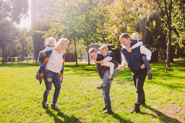 Thema familie actieve vrije tijd buiten in de natuur. grote blanke familie met vier kinderen. Pappa en mamma actief ontspannen. genieten van het leven in het park in de buurt van huis op gras. Kinderen op achterkant schouders roll bovenop — Stockfoto