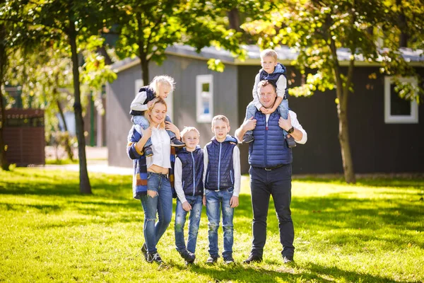 Téma rodiny aktivní trávení volného času venku v přírodě. Velká kavkazských rodina se čtyřmi dětmi. Máma a táta aktivně relaxační. užívat si života v parku u domu na trávě. Děti na zadní ramena najet na vrcholu — Stock fotografie