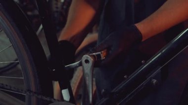 Tema küçük işletme bisiklet onarımı. Emanet giyen genç beyaz esmer adam gözlük, eldiven ve önlük tamir ve pedal sistemi Bisiklet garaj atölye ve krank ayarlama El aracını kullanır