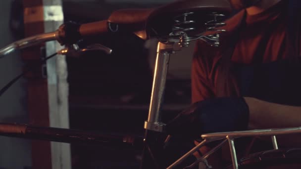 Тема малый бизнес ремонт велосипедов. Молодой кавказский брюнетка мужчина в защитных очках, перчатках и фартуке использует ручной инструмент для ремонта и регулировки велосипеда в мастерской гараж — стоковое видео