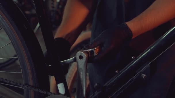 Tema pequeña empresa de reparación de bicicletas. joven caucásico morena hombre con gafas de seguridad, guantes y delantal utiliza herramienta de mano reparación y ajuste de manivela y pedal sistema de bicicleta en el taller de garaje — Vídeos de Stock