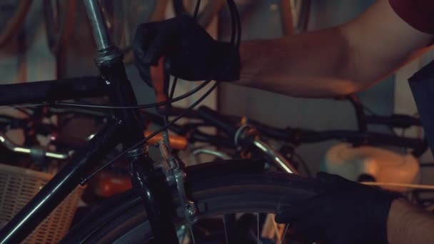 Tema pequeña empresa de reparación de bicicletas. Joven morena caucásica hombre en gafas protectoras, guantes y fartuhe utiliza herramientas de mano para reparar y afinar la llanta Frenos y bicicleta giratoria en un taller de garaje — Vídeo de stock