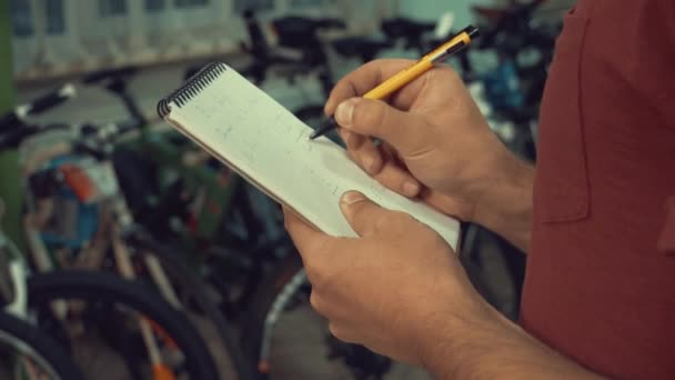 Тема малого бизнеса по продаже велосипедов. Молодой кавказский мужчина брюнетка владелец малого бизнеса, менеджер магазина использует блокнот и ручка делает заметки, контрольный список в магазине велосипедов — стоковое видео