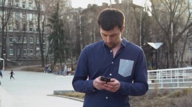 İnsan hakları ve sosyal SETI Tema. Molodoy beyaz adam elinde cep telefonu kullanarak, Sms Internet'i kullanan yazma, sohbet oturan sokakta yürüyen esmer rushke