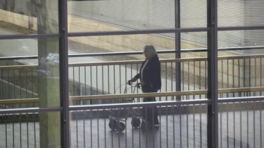 20 Ekim 2018. Krefeld Almanya. Tema tıp ve sağlık. Koridorda istasyonları arasındaki köprü boyunca içinde Walker'la kliniğinde yaşlı olgun beyaz Bayan hasta yürür. Pencereden görüntüleme