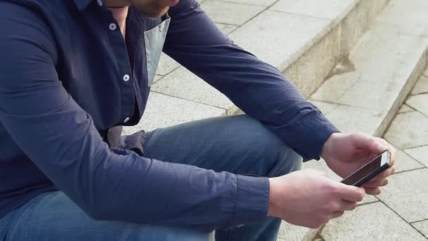 Το θέμα είναι ο άνθρωπος και τα κοινωνικά δίκτυα. νέοι Καυκάσιος λυπημένος αρσενικό μελαχρινή στο πουκάμισο είναι κάθεται στο πάρκο στο Letnec αναμονής, την αργοπορία χρησιμοποιεί χέρι να κρατήσει το κινητό τηλέφωνο. Συγκίνηση δυσαρέσκεια και διαταραχή — Αρχείο Βίντεο