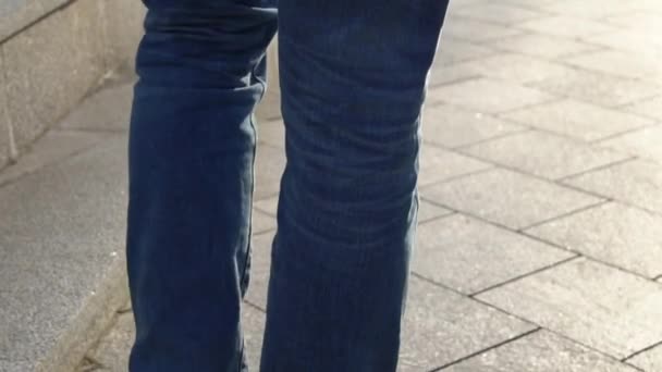 Primer plano de las piernas de un joven con zapatos rojos y vaqueros azules caminando por las escaleras de una calle de la ciudad en un clima soleado — Vídeo de stock