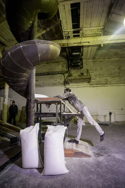 El tema es una fábrica de trabajo. Un hombre caucásico lleva bolsas pesadas de productos terminados en una antigua fábrica. Trabajo físico en producción en los países postsoviéticos . — Foto de Stock