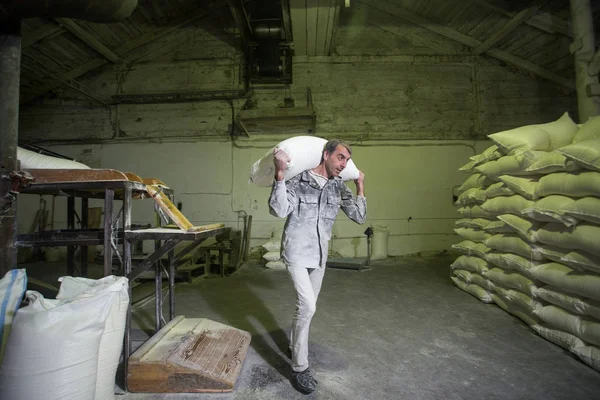 El tema es una fábrica de trabajo. Un hombre caucásico lleva bolsas pesadas de productos terminados en una antigua fábrica. Trabajo físico en producción en los países postsoviéticos . —  Fotos de Stock