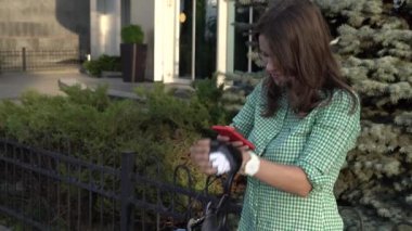 Genç beyaz kız öğrenci el holding telefon dokunmatik ekran için kullanır. Bir kadın bir kiralama şehir bisikleti bir kask ve gömlek bir kaldırımda güneşli havalarda durumda. Mola mola
