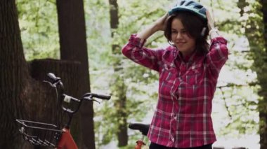 Denek ekolojik ulaşım bisikleti. Mavi kasklı, uzun saçlı, turuncu renkli bir bisikletin yanında duran, şehir parkında sepeti olan güzel, beyaz bir kadın.