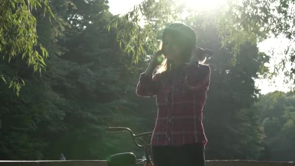 Thema ökologisches Verkehrsmittel Fahrrad. Die schöne junge Frau mit blauem Helm und langen Haaren posiert in einem Stadtpark neben einem orangefarbenen Leihfahrrad mit Korb. — Stockvideo