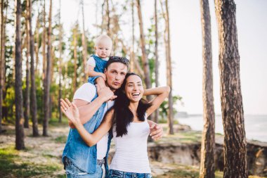 Aile anne, baba ve kızı oturur baba omuzlarında ve veliler ormandaki niteliğine yaz gün batımında öpücük