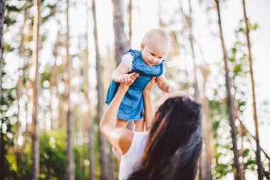 Anneler günü. Güzel bir genç Kafkas kadın anne ellerinin üzerinde tutan asansörler üzerinde ellerini kızı yukarı kadar yaz aylarında ormanda atar. Anne ve çocuk doğa orman Park