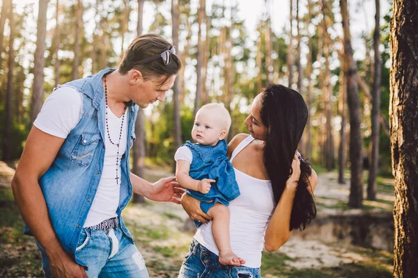 a family of three, young beautiful parents playing with their daughter sitting on the shoulders of the pope one year after birth in the coniferous forest in summer