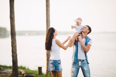 Deniz Manzaralı Aile Açık Rekreasyon. Genç Kafkas ailesi kollarında bir yaşında çocukla, dinlenme, şık denim giysileri bütün gün kapalı, turizm tatil, cliff doruk noktasıydı bakın deniz