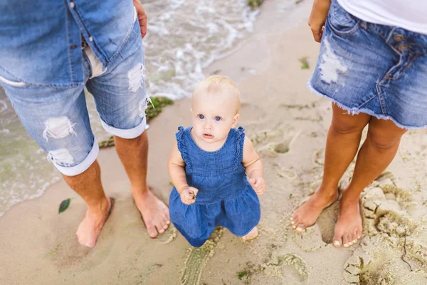 Joven pareja heterosexual familiar. Mamá y papá caucásicos están aprendiendo a caminar un niño pequeño cogido de la mano de un niño en una playa de arena cerca del mar. Vacaciones en familia en la playa, caminar descalzo en la naturaleza —  Fotos de Stock