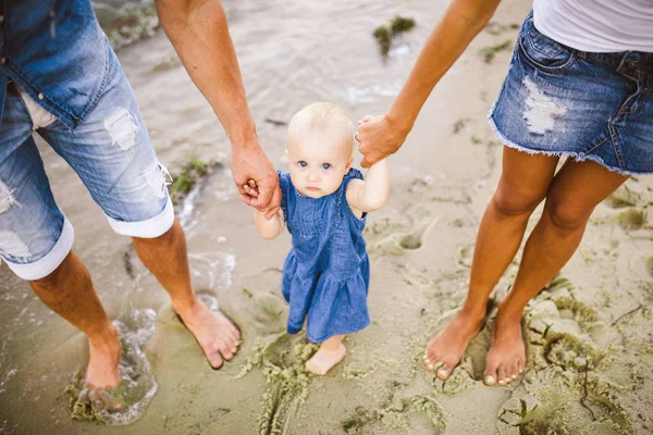 Joven pareja heterosexual familiar. Mamá y papá caucásicos están aprendiendo a caminar un niño pequeño cogido de la mano de un niño en una playa de arena cerca del mar. Vacaciones en familia en la playa, caminar descalzo en la naturaleza —  Fotos de Stock