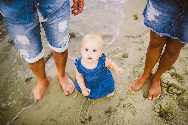 Joven pareja heterosexual familiar. Mamá y papá caucásicos están aprendiendo a caminar un niño pequeño cogido de la mano de un niño en una playa de arena cerca del mar. Vacaciones en familia en la playa, caminar descalzo en la naturaleza —  Fotos de Stock